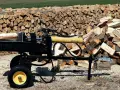 Czarna piło łuparka z żółtym cylindrem hydraulicznym stoi obok stosów drewna opałowego.