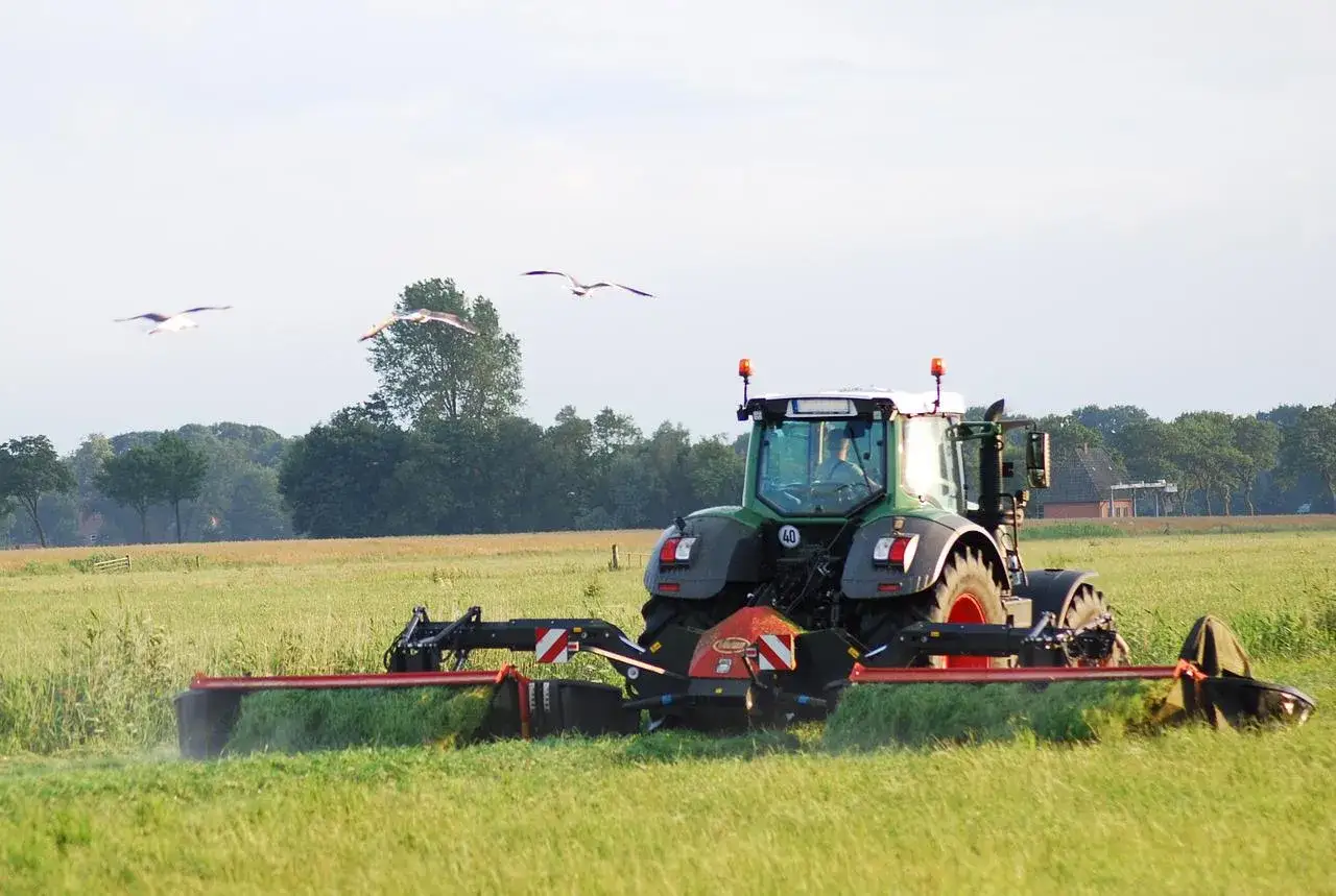Zielony traktor z zamontowanym dyskiem koszącym, kt&oacute;ry jest napędzany przez wałek przekazu mocy, pracuje na zielonym polu.
