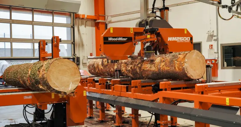 Pomarańczowa maszyna do obróbki drewna Wood-Mizer WM2500 przetwarza pień drzewa na deski.